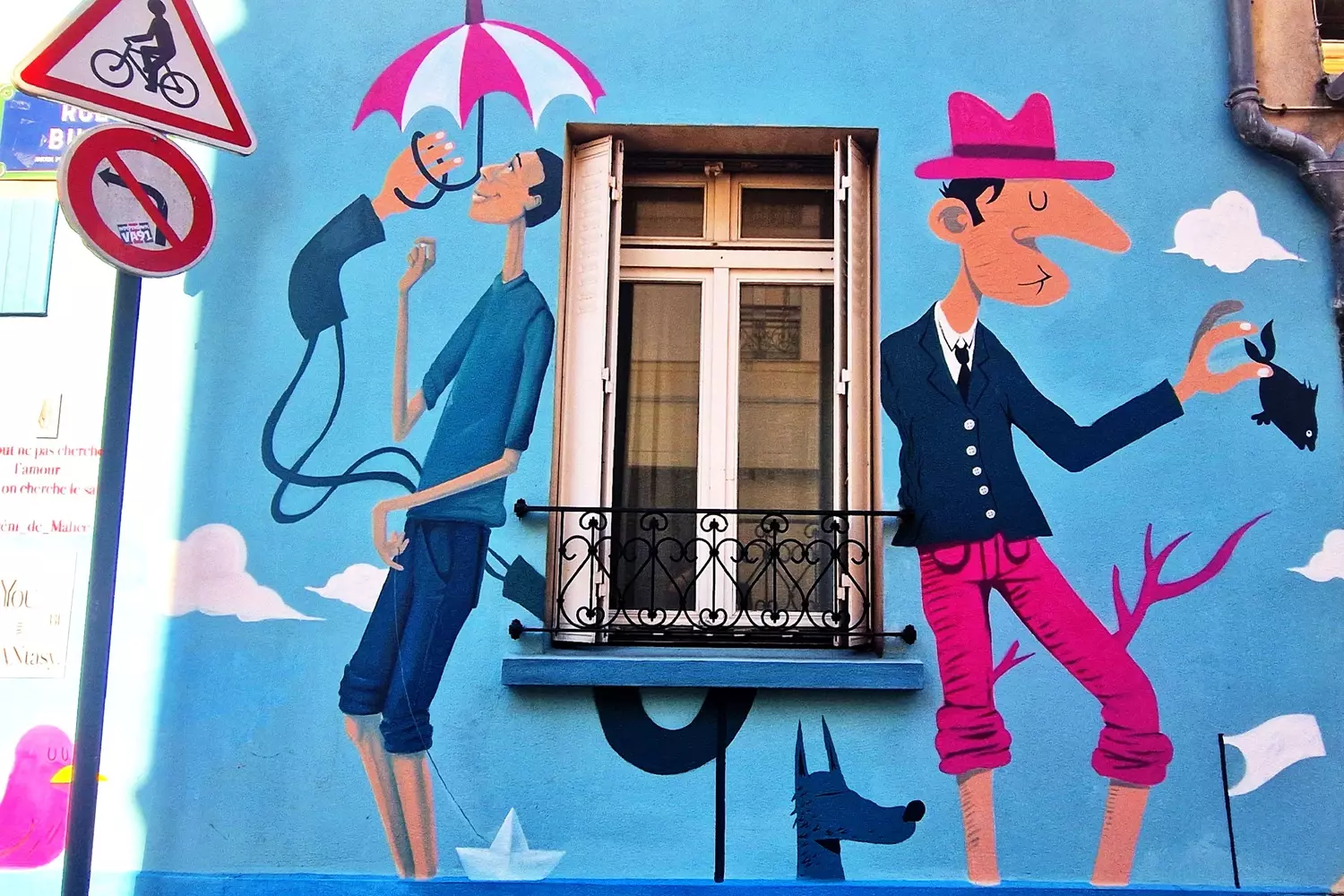 Fresque colorée de deux personnages souriants autour d'une fenêtre, sur un mur bleu de la Butte-aux-Cailles