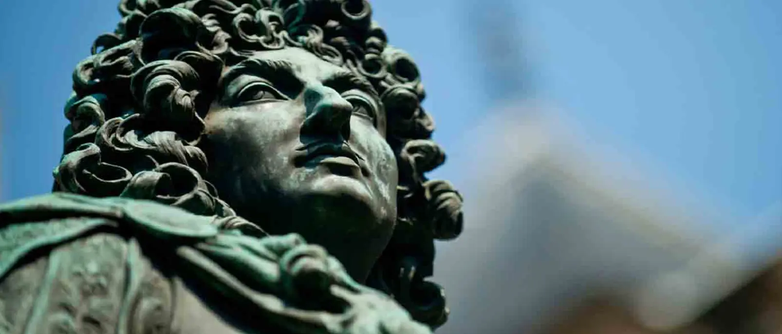 Visage en bronze patiné de Louis XIV coiffé d'une perruque bouclée, en gros plan