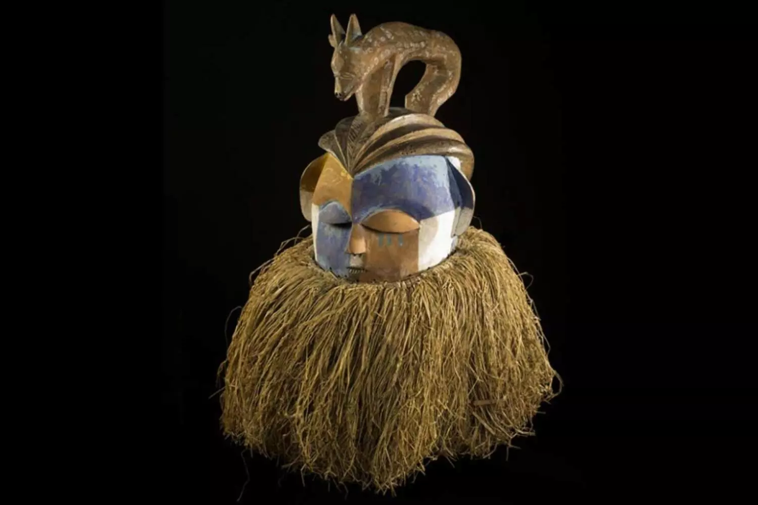 Masque africain surmonté d'une antilope sculptée, avec une collerette de fibres, sur fond noir