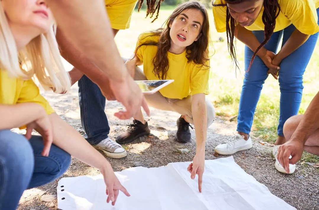 Équipe en tee-shirts jaunes accroupie autour d'une carte lors d'un jeu de piste en plein air