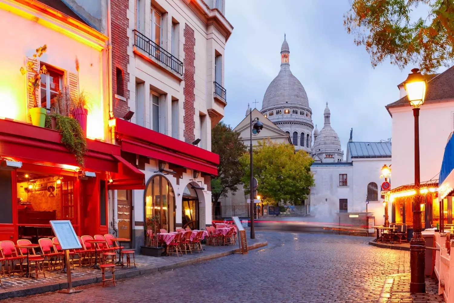 Cobbled street in Montmartre lined with red-awning cafés, the Sacré-Cœur in the background