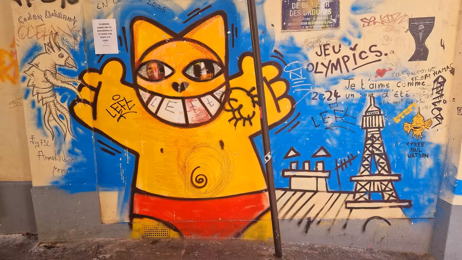 Chat jaune souriant de M. Chat peint sur un mur couvert de graffitis, à Montmartre