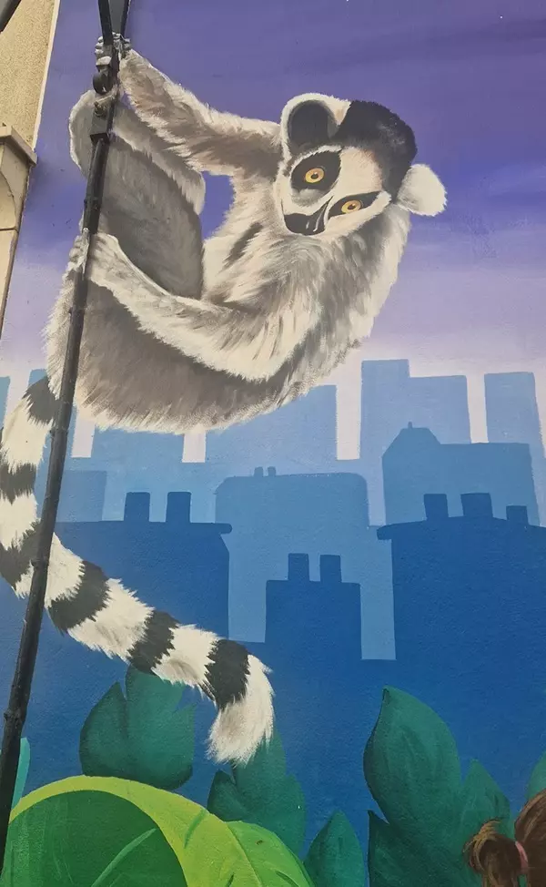 Fresque de street art d'un lémurien accroché à une liane au-dessus des toits de la ville