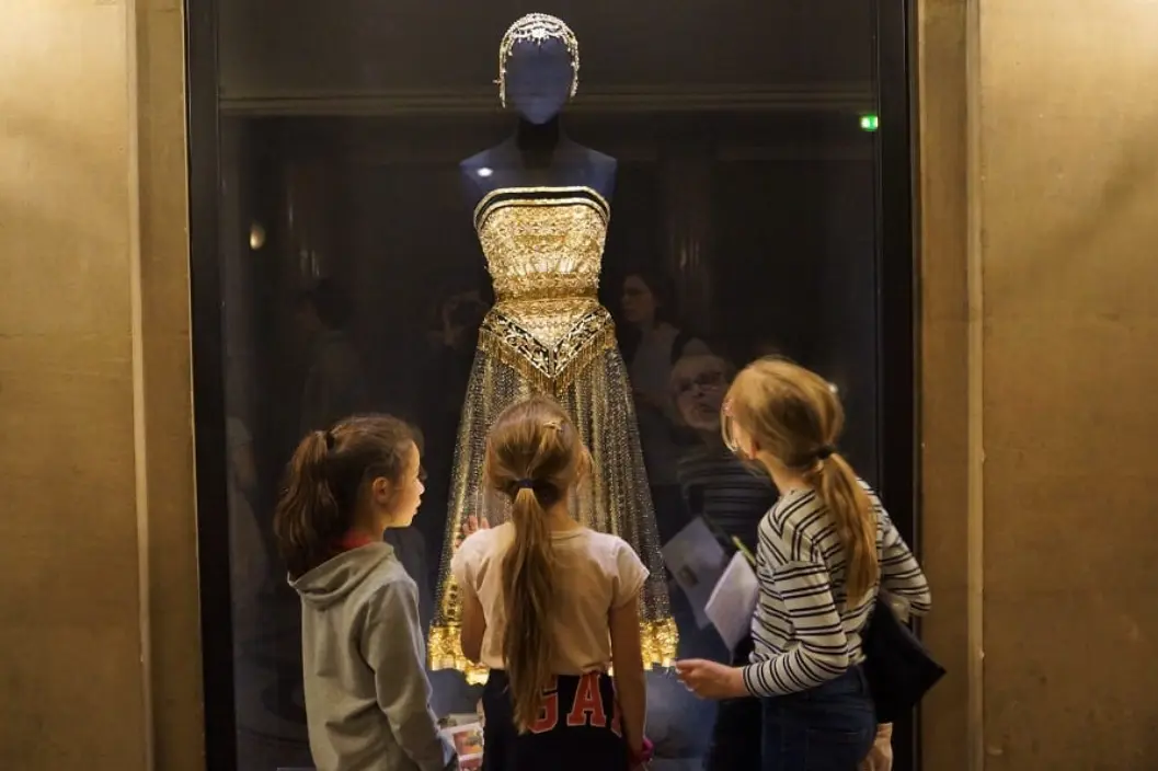 Trois fillettes devant une vitrine présentant un costume de scène doré, au Palais Garnier