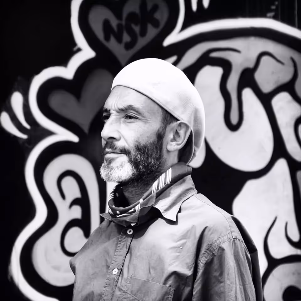Portrait en noir et blanc de Sigismond, guide en casquette, devant un mur de graffitis