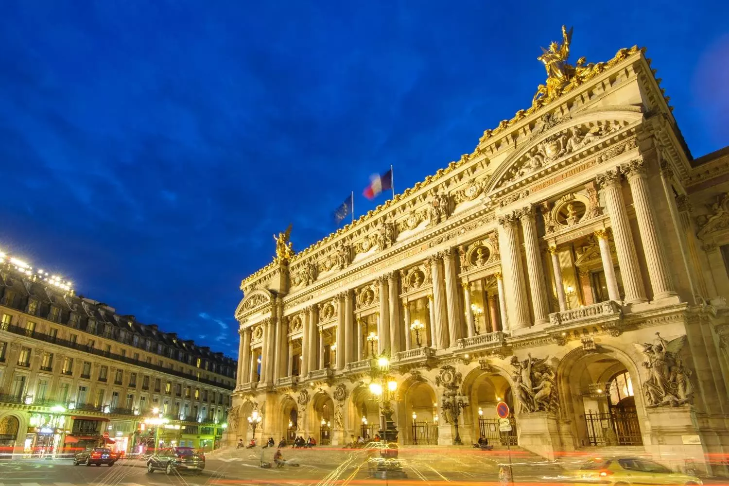 Illuminated facade of the Palais Garnier at nightfall, under a deep blue sky