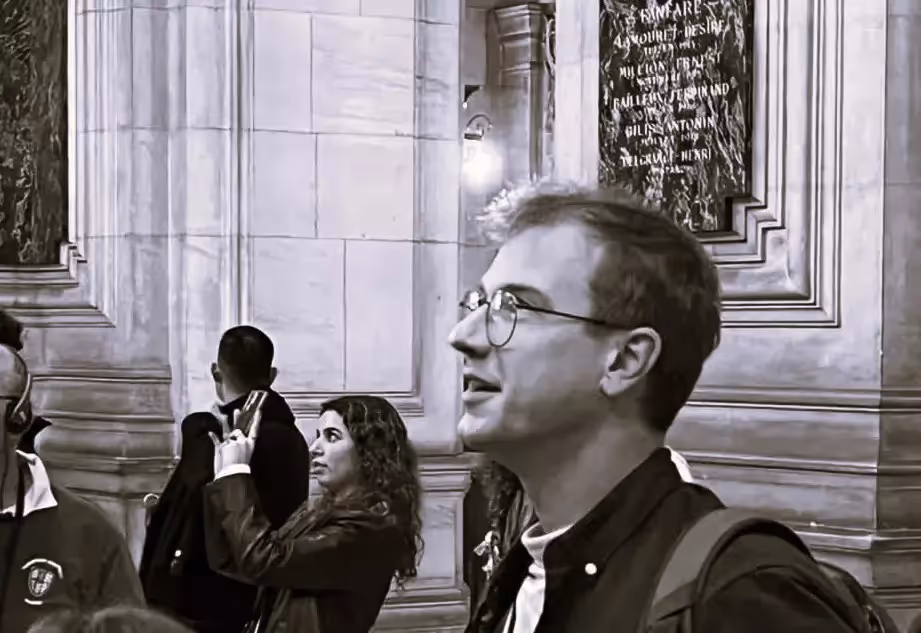 Thomas, guide, levant les yeux avec un groupe de visiteurs dans un édifice, photo en noir et blanc
