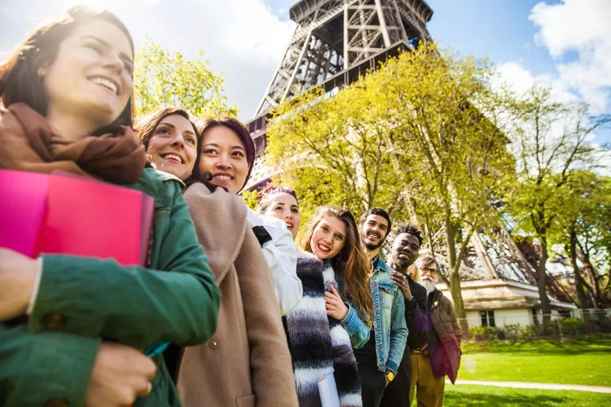 Groupe de jeunes adultes souriants dans un parc au pied de la tour Eiffel