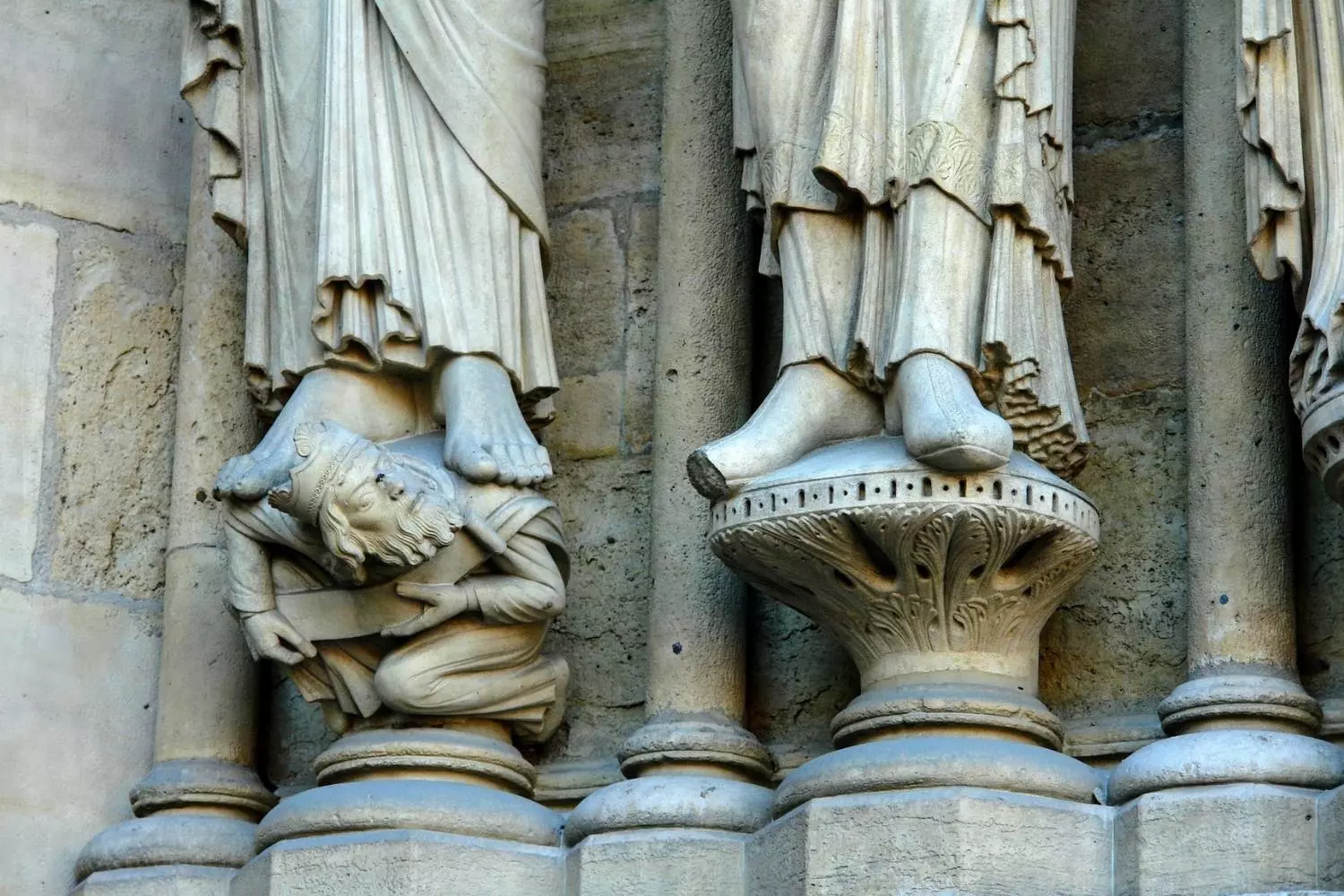Feet of saint statues resting on small carved figures, on the portal of Notre-Dame de Paris