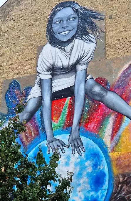 Fresque de street art d'une fillette souriante qui saute par-dessus un globe terrestre
